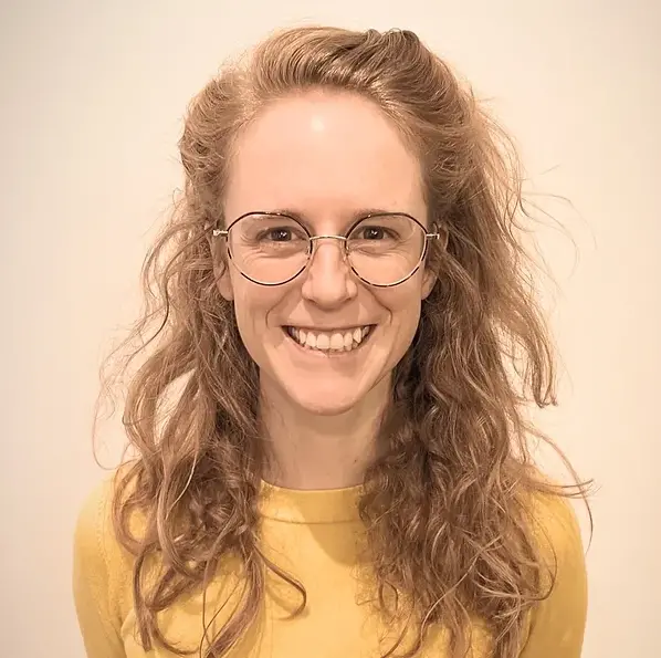 A smiling woman in her mid-thirties, wearing glasses and a yellow shirt.